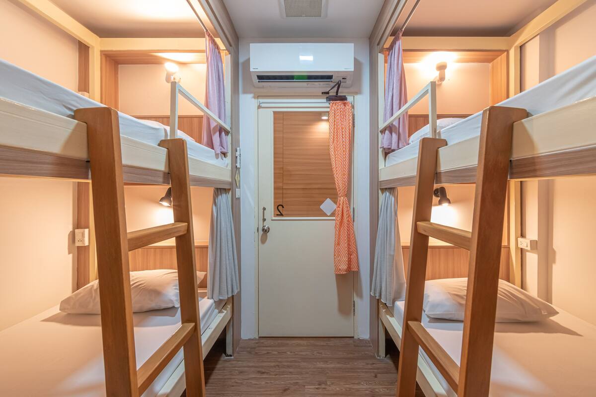 A narrow hallway with bunk beds on either side, a door at the end, and an air conditioning unit above.