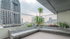 A balcony with a concrete bench, potted plants, and a view of tall buildings. - The Victory View - Hostel - Adults only (Bangkok)
