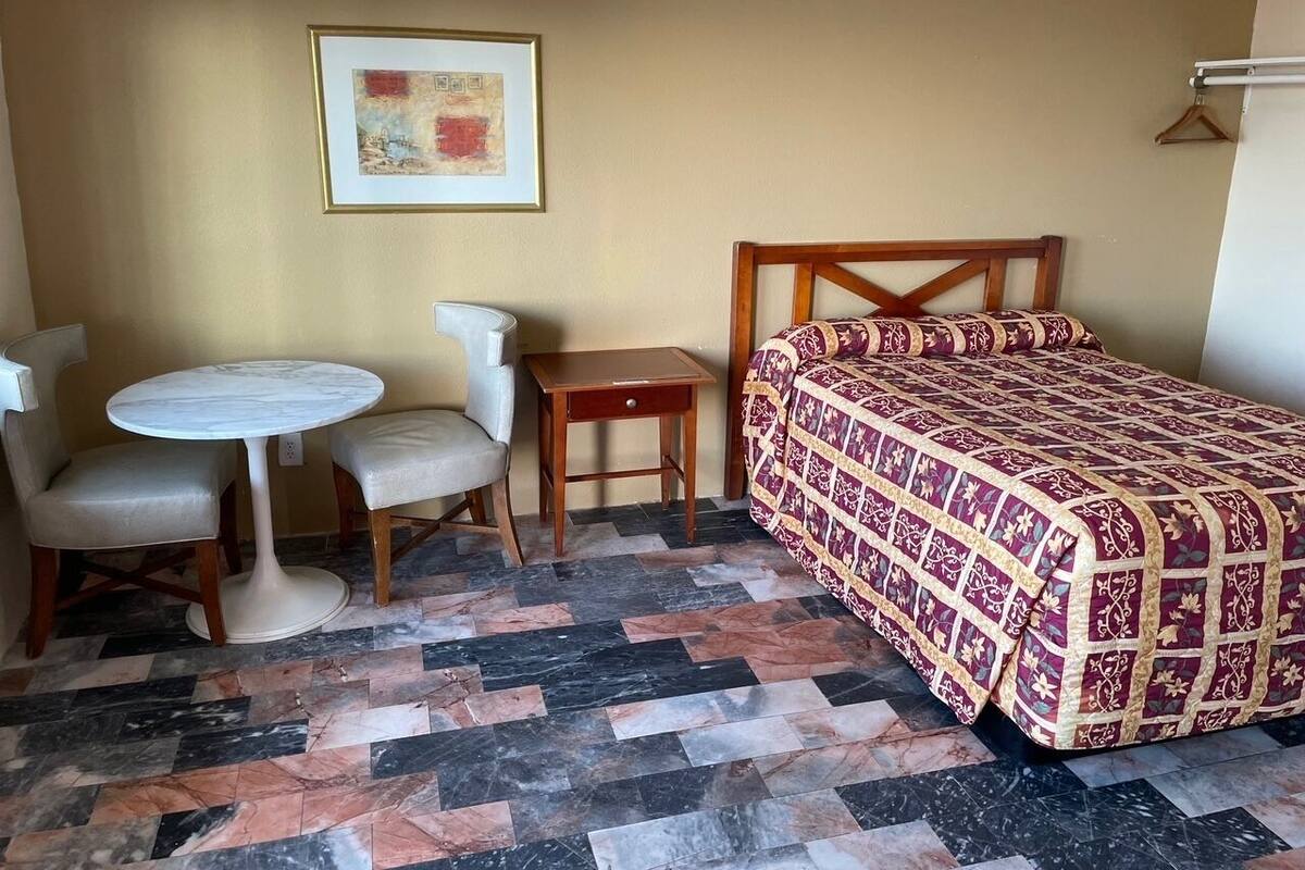A room with a bed, two chairs, a small table, and a framed picture on the wall.