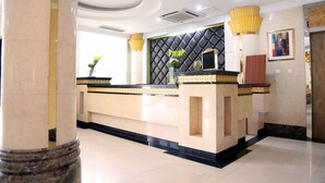A reception area with a marble counter, a black and gold decorative wall, and a framed portrait on the wall. - Hotel Amaritsah (Brazzaville)