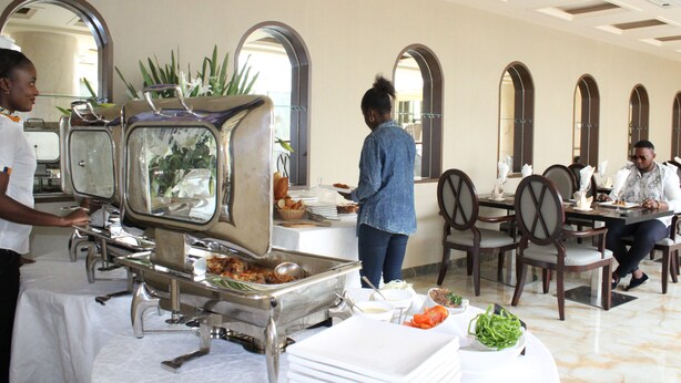 A buffet setup with multiple serving stations, a dining area with tables and chairs, and a ceiling with a grid pattern. - Hotel Amaritsah (Brazzaville)