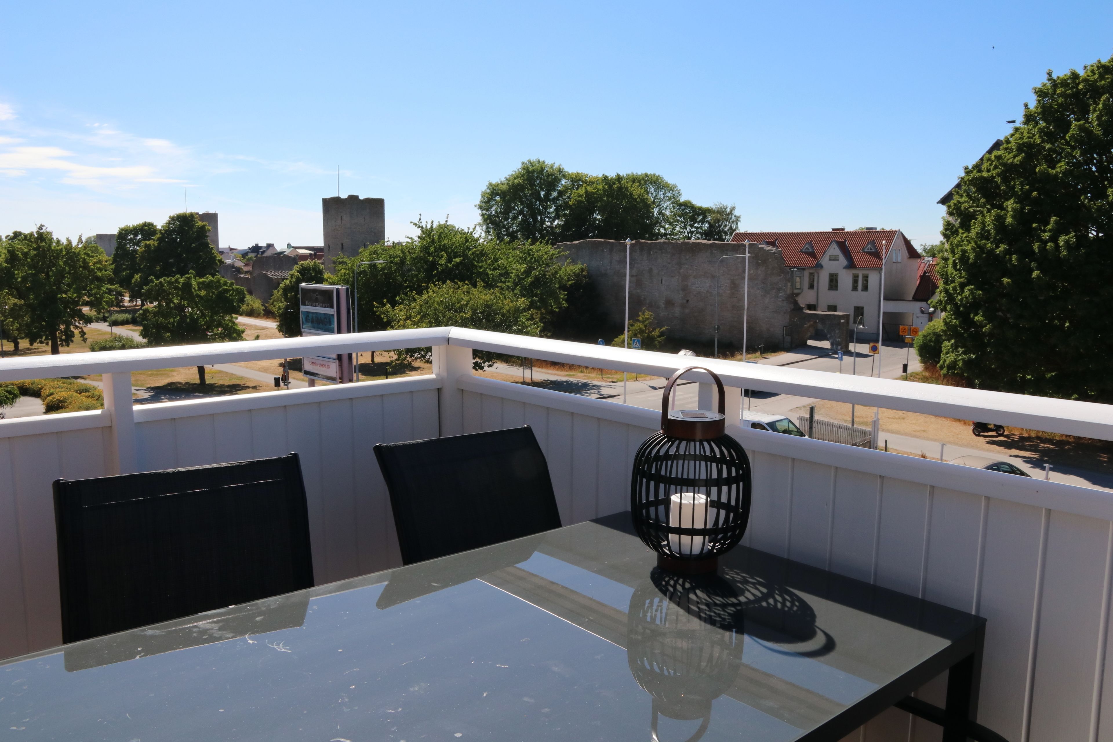 Ein Balkon mit Glastisch, schwarzen Stühlen und einer Laterne.