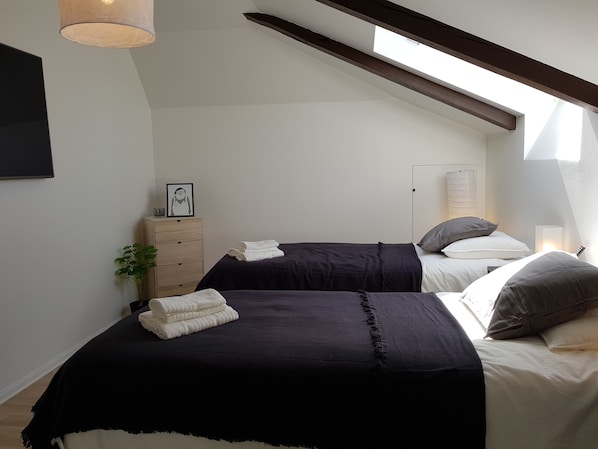 Un dormitorio con dos camas, un aparador de madera, un cuadro enmarcado y un tragaluz.