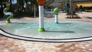 Un élément décoratif aquatique comprenant un toboggan en spirale et deux fontaines sphériques, situé dans une cour bordée de palmiers, avec un bâtiment en arrière-plan.
