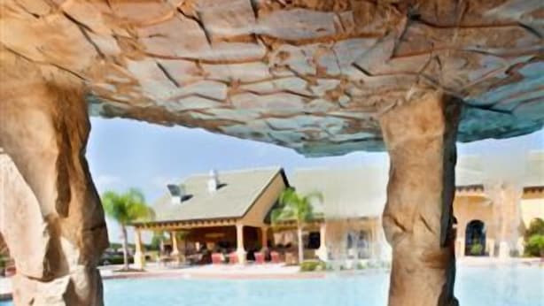 Un bain à remous doté d’un toit en pierre, entouré d’un espace piscine avec des chaises longues et un bâtiment visible au loin.