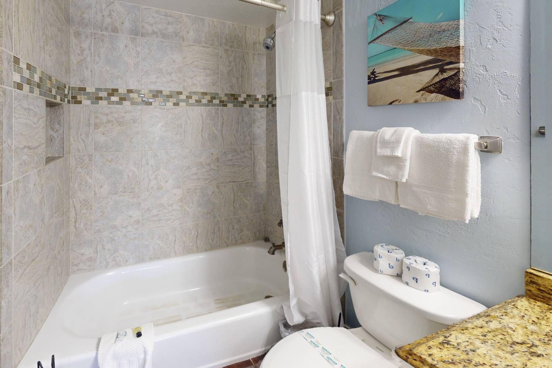 A bathroom with a bathtub, toilet, and shower curtain. There are two rolls of toilet paper on the toilet tank.
