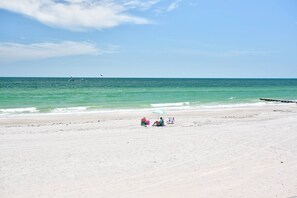 A beach with a clear sky, calm sea, and a few people relaxing. - Spectacular Beachfront Corner Unit w/ Views, Pool and Great Location on Madeira Beach (Madeira Beach)