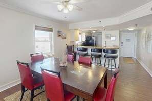 A dining area with a wooden table and red chairs, a kitchen in the background, and a ceiling fan. - Spectacular Beachfront Corner Unit w/ Views, Pool and Great Location on Madeira Beach (Madeira Beach)