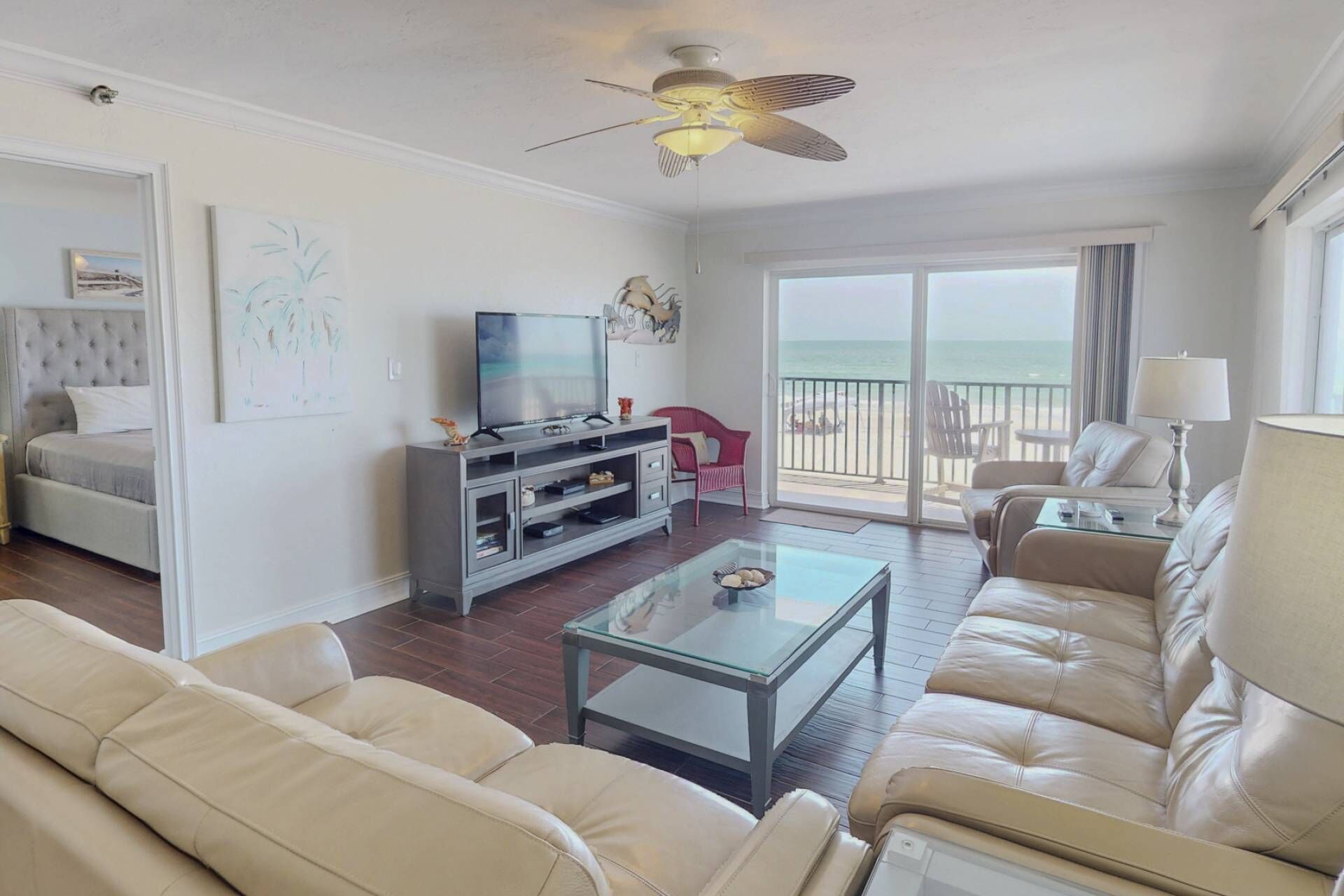 A spacious living room with a large sofa, a coffee table, a TV, and a balcony with a view of the ocean.