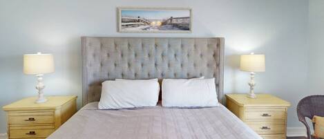 A bedroom with a tufted headboard, two bedside tables with lamps, a bed with white linens, and a framed picture above the headboard.