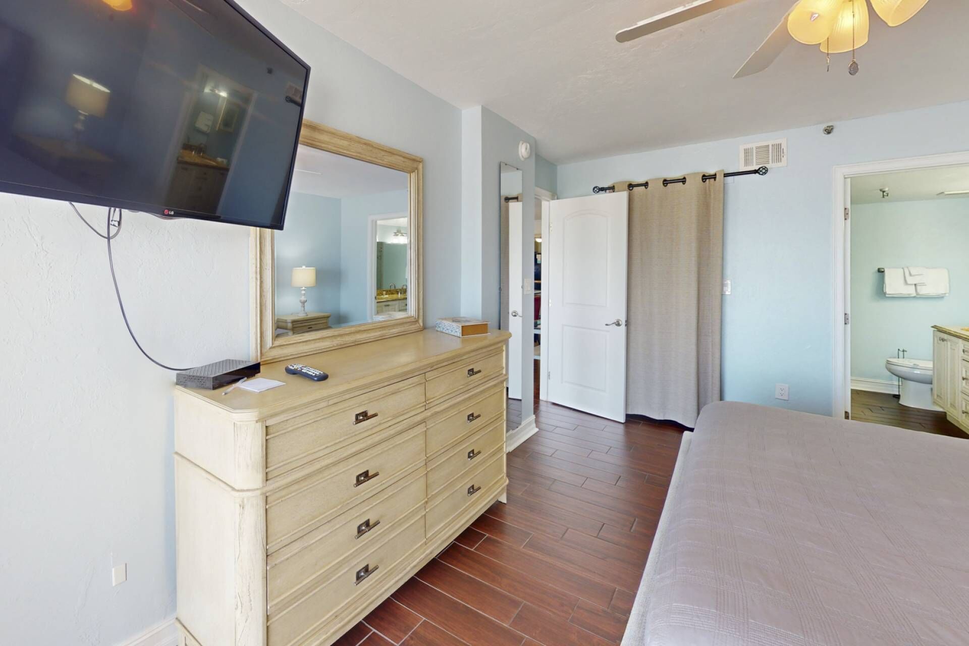 Une chambre à coucher avec un lit, une commode, un téléviseur et une salle de bain visible à travers une porte ouverte.
