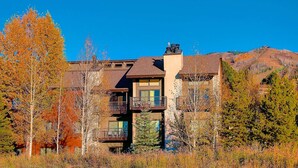 A modern multi-story building with a balcony on the second floor, surrounded by autumn foliage. - Mtn Views-Heated Pool-HotTub-Grill-Deck+Walk to Mtn/Trails/Resort/Eat/Drink/Free Town Bus-Immaculate (Steamboat Springs)
