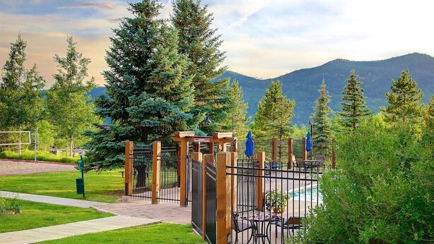 A gated entrance to a park with a pool area, surrounded by tall trees and mountains in the background. - Mtn Views-Heated Pool-HotTub-Grill-Deck+Walk to Mtn/Trails/Resort/Eat/Drink/Free Town Bus-Immaculate (Steamboat Springs)