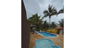 A swimming pool with a slide, surrounded by palm trees and a stone patio.