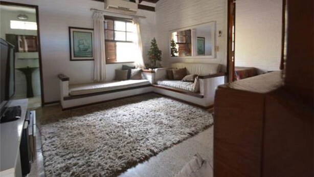 A living room with a built-in bench, a large rug, a potted plant, and a mirror on the wall.