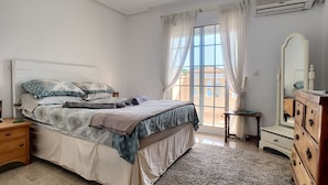 Ein Schlafzimmer mit Bett, Schminktisch, Nachttisch und einem Fenster mit Vorhängen.