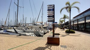 Ein Yachthafen mit mehreren vertäuten Booten, ein hölzernes Wegweiser mit verschiedenen Firmennamen und ein modernes Gebäude mit großen Fenstern auf der rechten Seite.