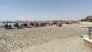 Ein Strand mit Liegestühlen und Sonnenschirmen, ein sandiger Uferstreifen und ein klarer Himmel.