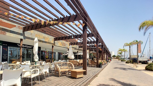 Ein Straßencafé mit Holztischen und -stühlen, Sonnenschirmen und einer Holzpergola.