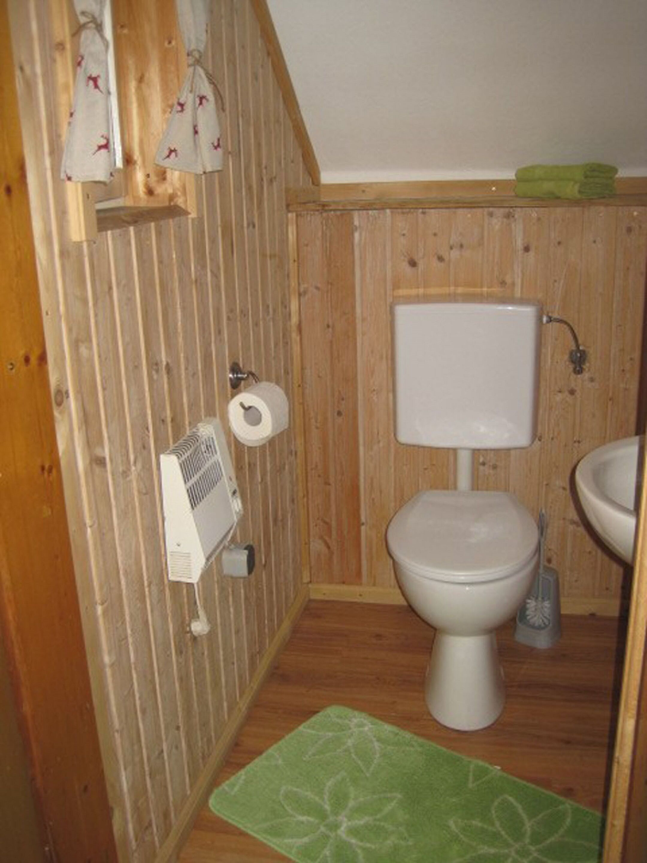 A small, wooden-paneled bathroom with a toilet, sink, and a green mat on the floor.