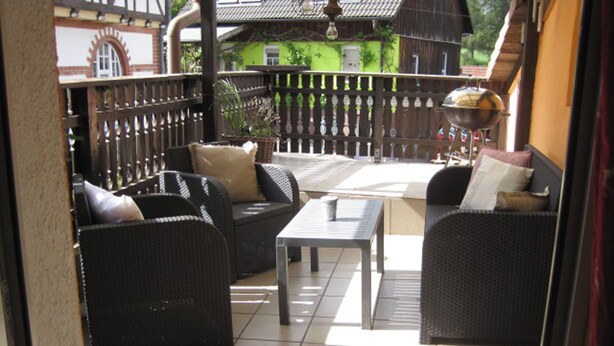 A patio area with wicker furniture, a table, and a grill. - Ferienhaus Becker (Roedental)