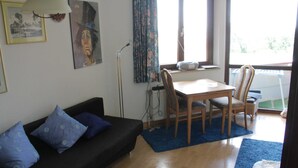 A living room with a dark sofa, blue cushions, a wooden dining table with chairs, a lamp, and a window with curtains. - Apartment at the harbor, Germany (Lübeck)