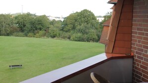 A balcony with a view of a grassy lawn and trees, a brick wall, and a wicker chair. - Apartment at the harbor, Germany (Lübeck)