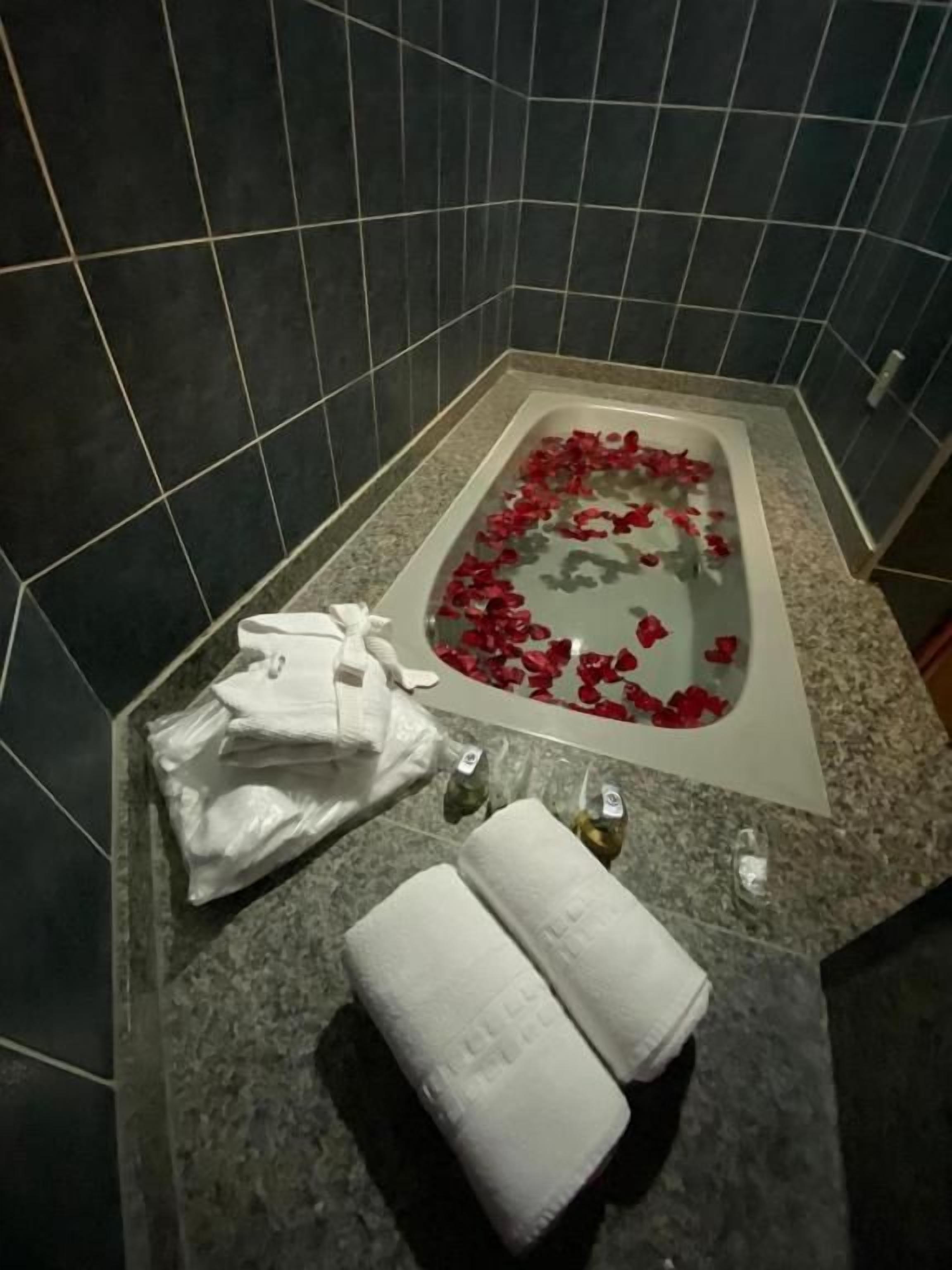 A bathroom with a bathtub, towels, and rose petals on the floor.