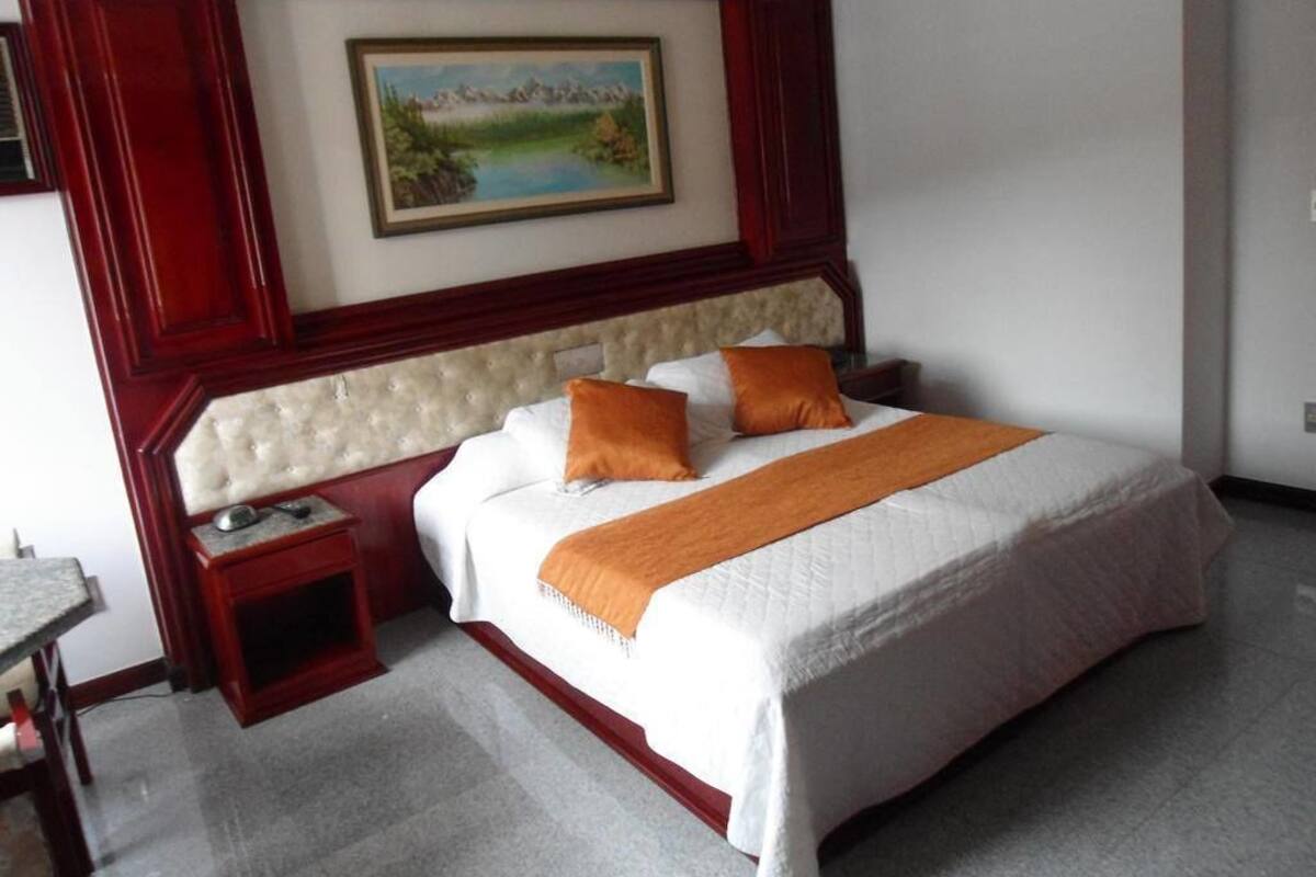 Una habitación de hotel con una cama grande, una mesita de noche, un cuadro en la pared y una pequeña mesa.