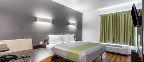 Quarto de hotel moderno com uma cama, uma escrivaninha, uma cadeira, uma televisão e uma janela com cortinas.