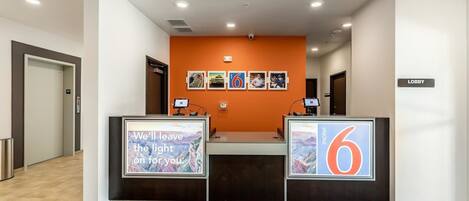 A hotel reception area with a modern design, featuring a reception desk, a digital display, and a series of framed pictures on the wall.