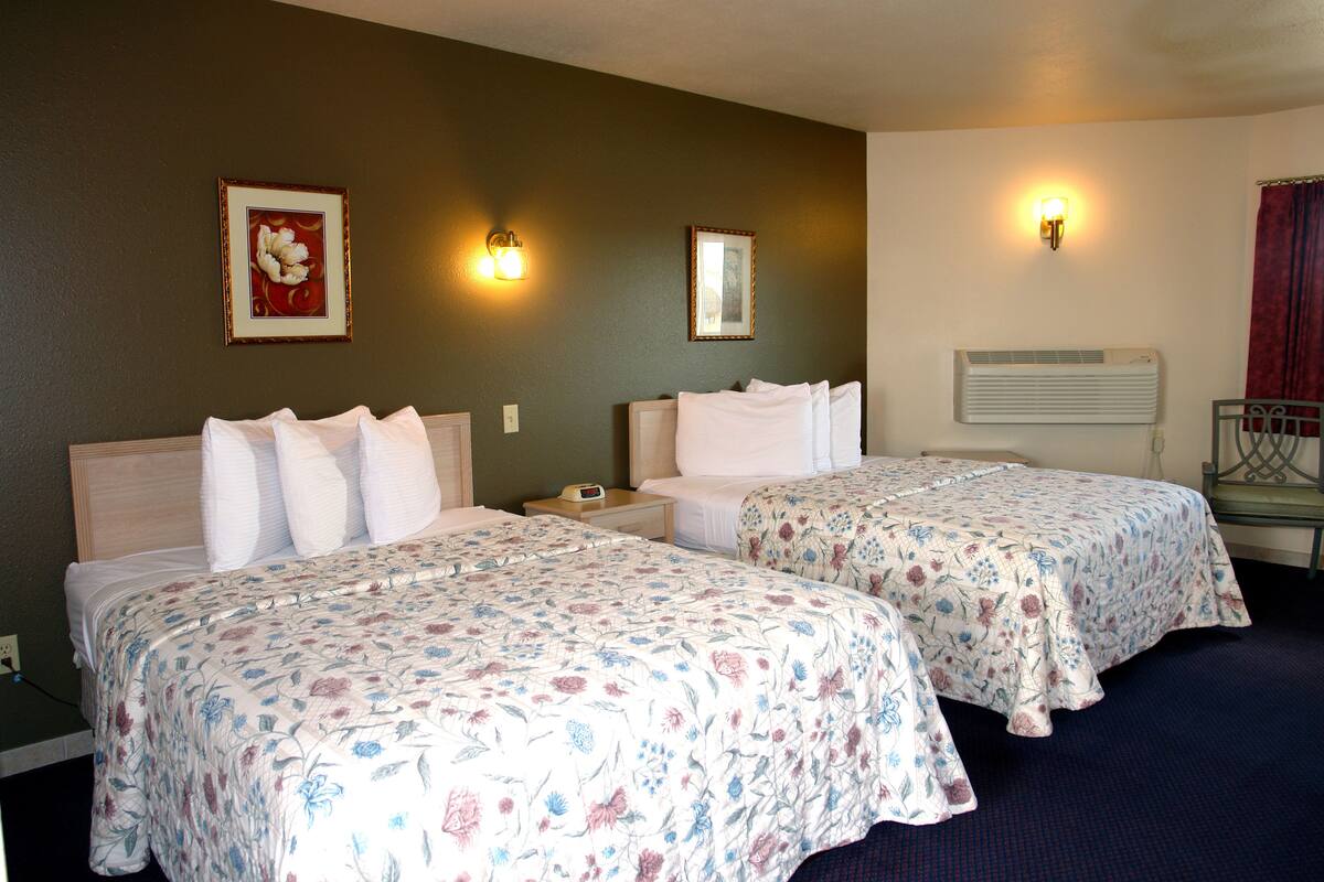 A hotel room with two beds, a nightstand, a wall-mounted air conditioner, and two wall sconces.