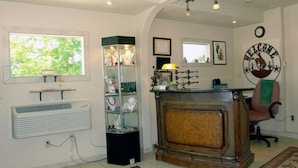 A reception area with a wooden desk, a glass display case with jewelry, a wall clock, and a welcome sign. - Carter Mountain Motel (Cody)