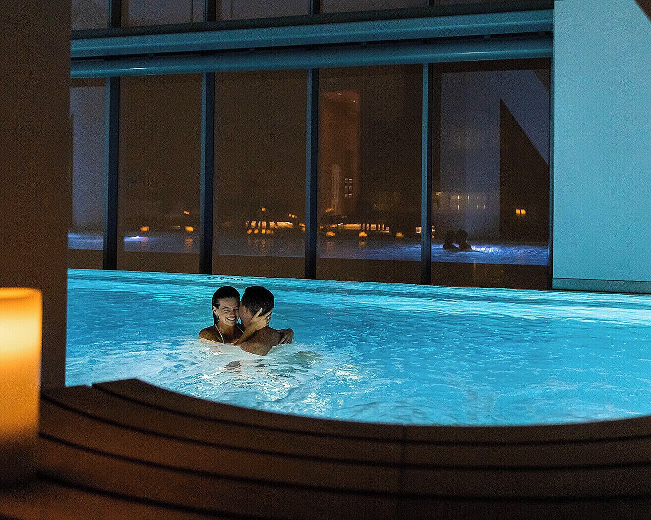 A couple in a hot tub with a city view at night.