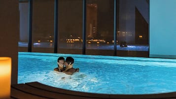 Una pareja en un jacuzzi con vistas a la ciudad por la noche.