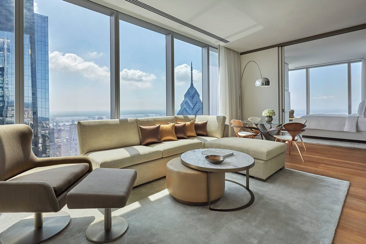 Ein modernes Hotelzimmer mit großem Fenster, einer Couch, einem runden Couchtisch und einem Bett.