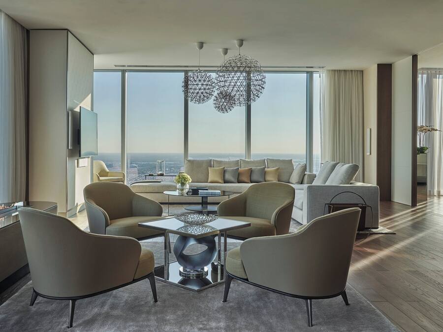 A modern living room with a large window, a sofa, two armchairs, a coffee table, and a decorative light fixture.