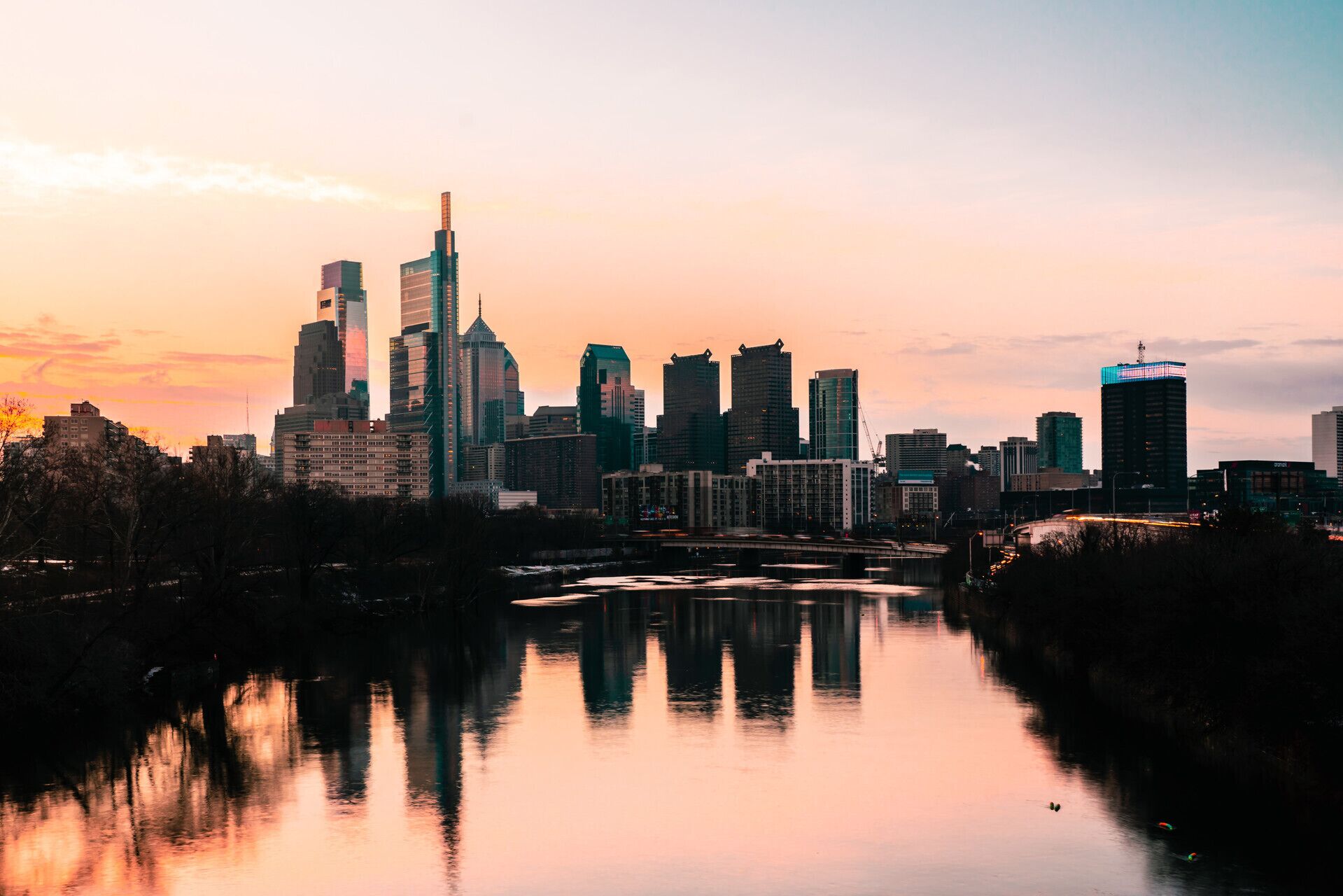 A city skyline at sunset with a river reflecting the buildings.