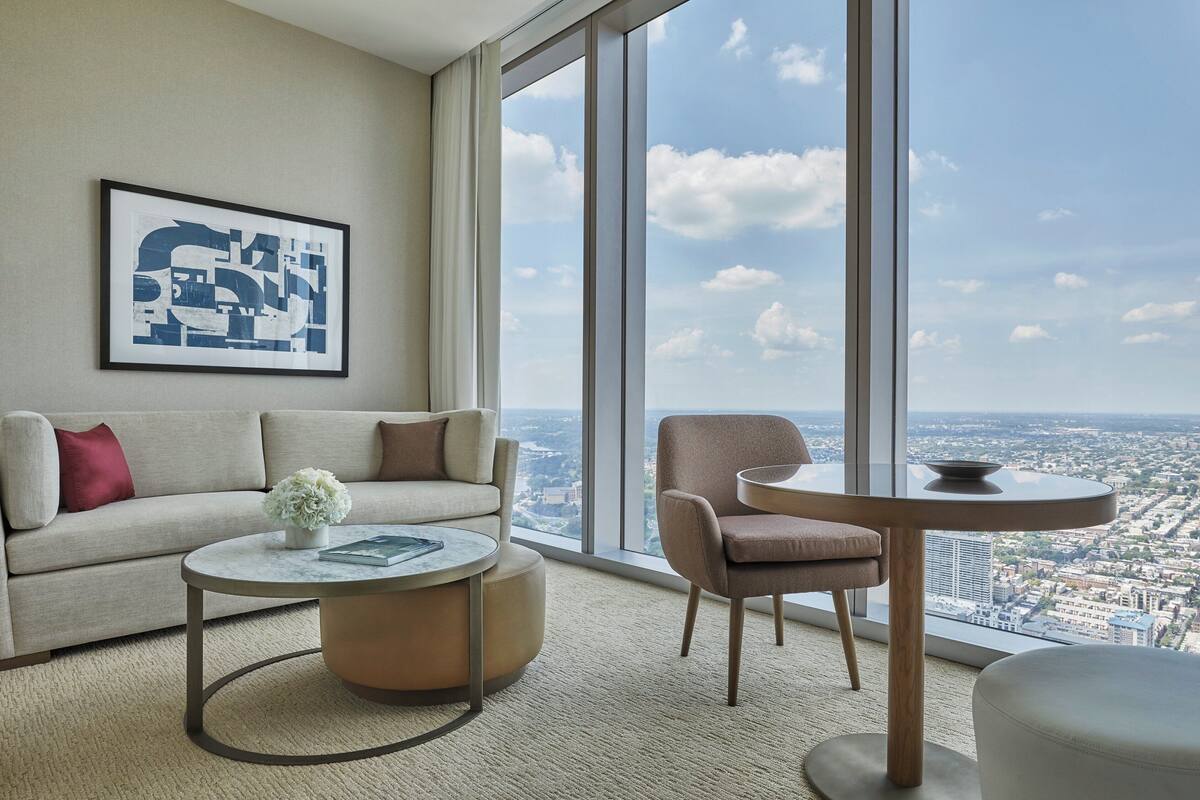 Ein modernes Wohnzimmer mit Sofa, Sessel, Couchtisch und einem großen Fenster mit Blick auf die Stadt.