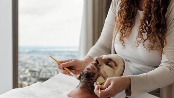 Uma pessoa recebendo tratamento facial em um quarto com uma janela grande com vista para a cidade.
