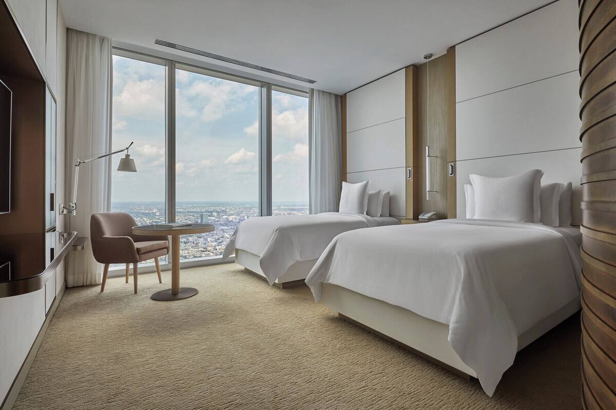 Ein modernes Hotelzimmer mit zwei Betten, einem Schreibtisch und einem Stuhl.