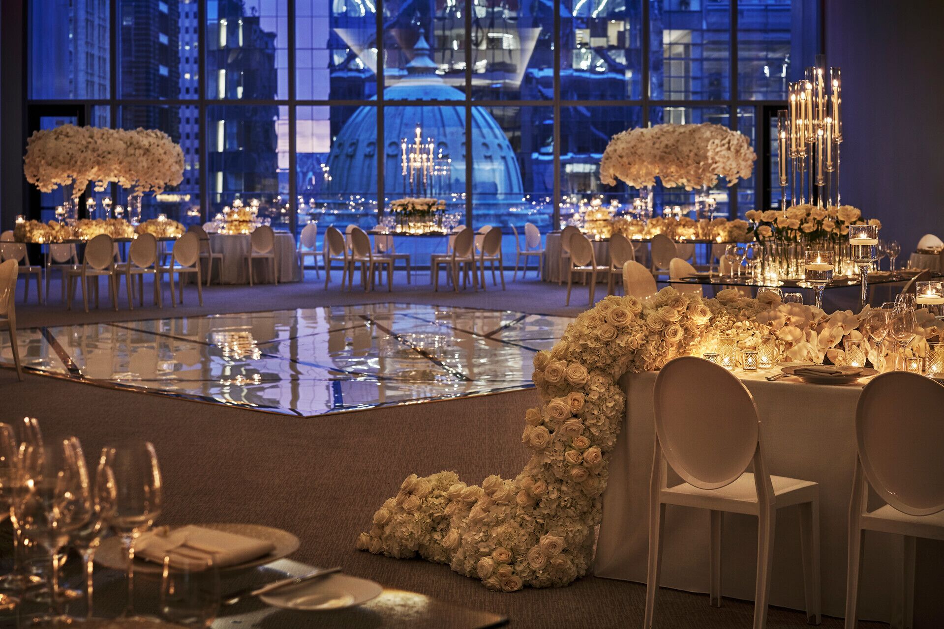 A formal dining area with tables set for a banquet, featuring floral centerpieces and candle lighting.
