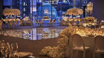 A formal dining area with tables set for a banquet, featuring floral centerpieces and candle lighting.