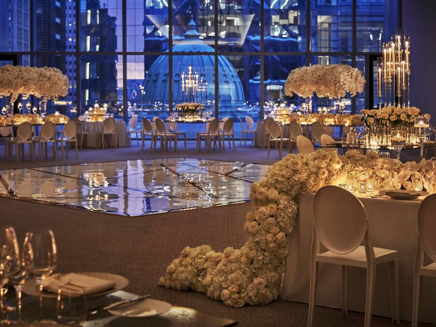 A formal dining area with tables set for a banquet, featuring floral centerpieces and candle lighting.