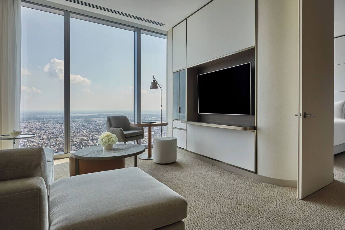 Ein modernes Hotelzimmer mit großem Fernseher, einer gemütlichen Sitzecke und Blick auf die Stadt.