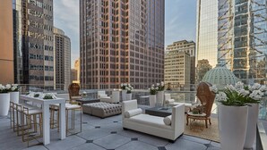 Eine Dachterrasse mit moderner Möbel, üppigen Kübelpflanzen und Blick auf die Stadt.