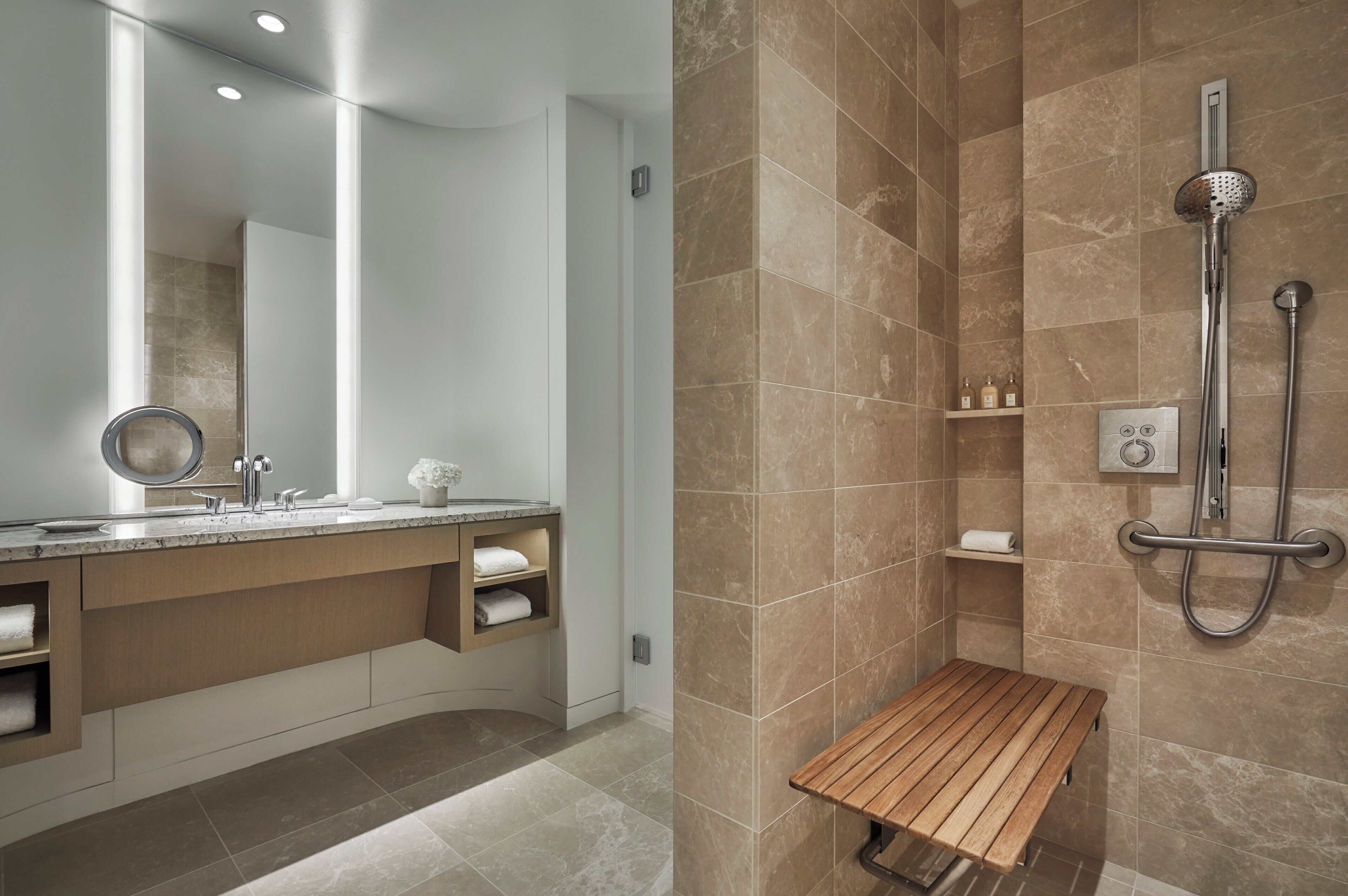 Een moderne badkamer met een grote spiegel, een houten bankje, een douche met handdouche en een handdoekrek.