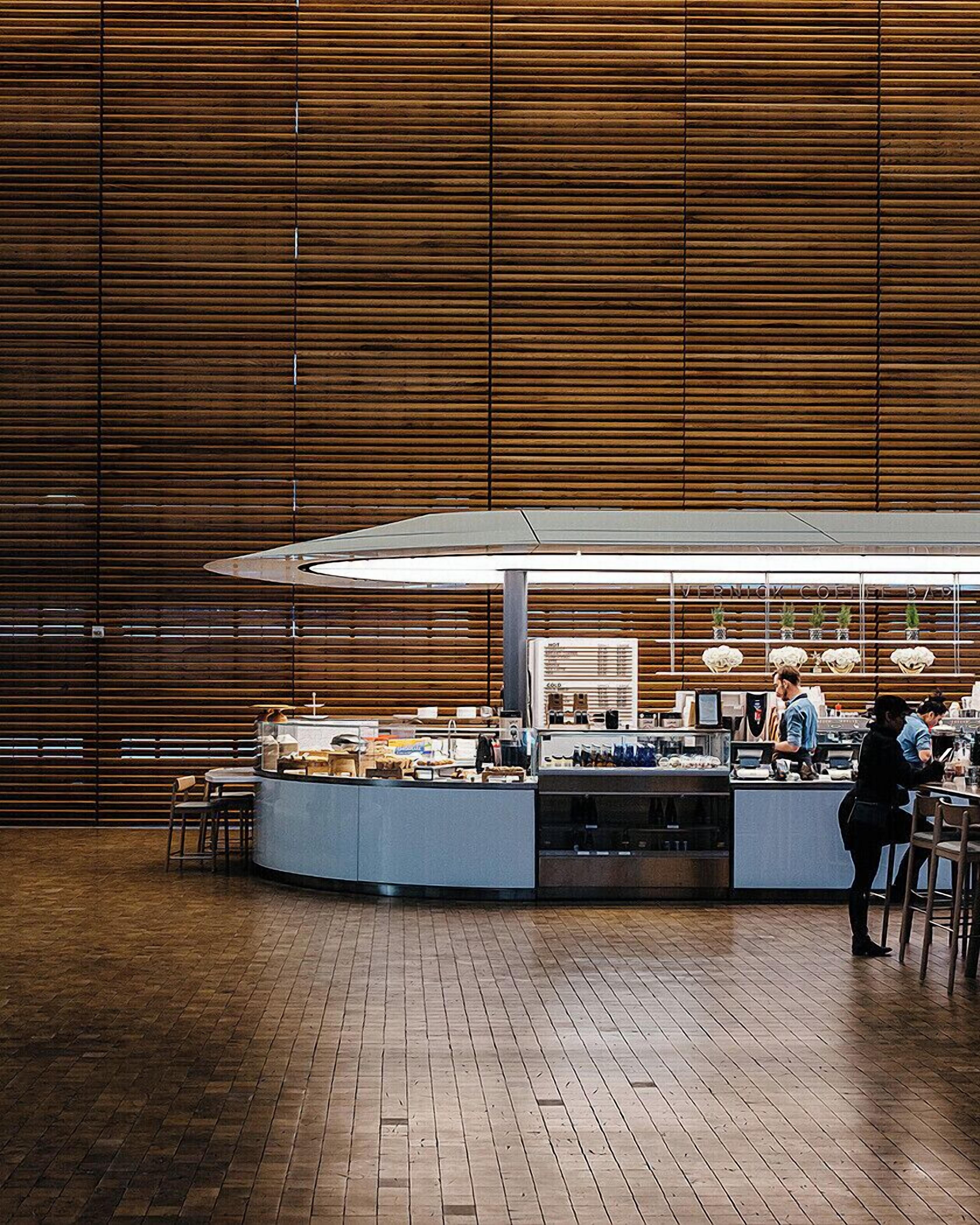 A modern café with a wooden interior, a central counter, and seating areas.