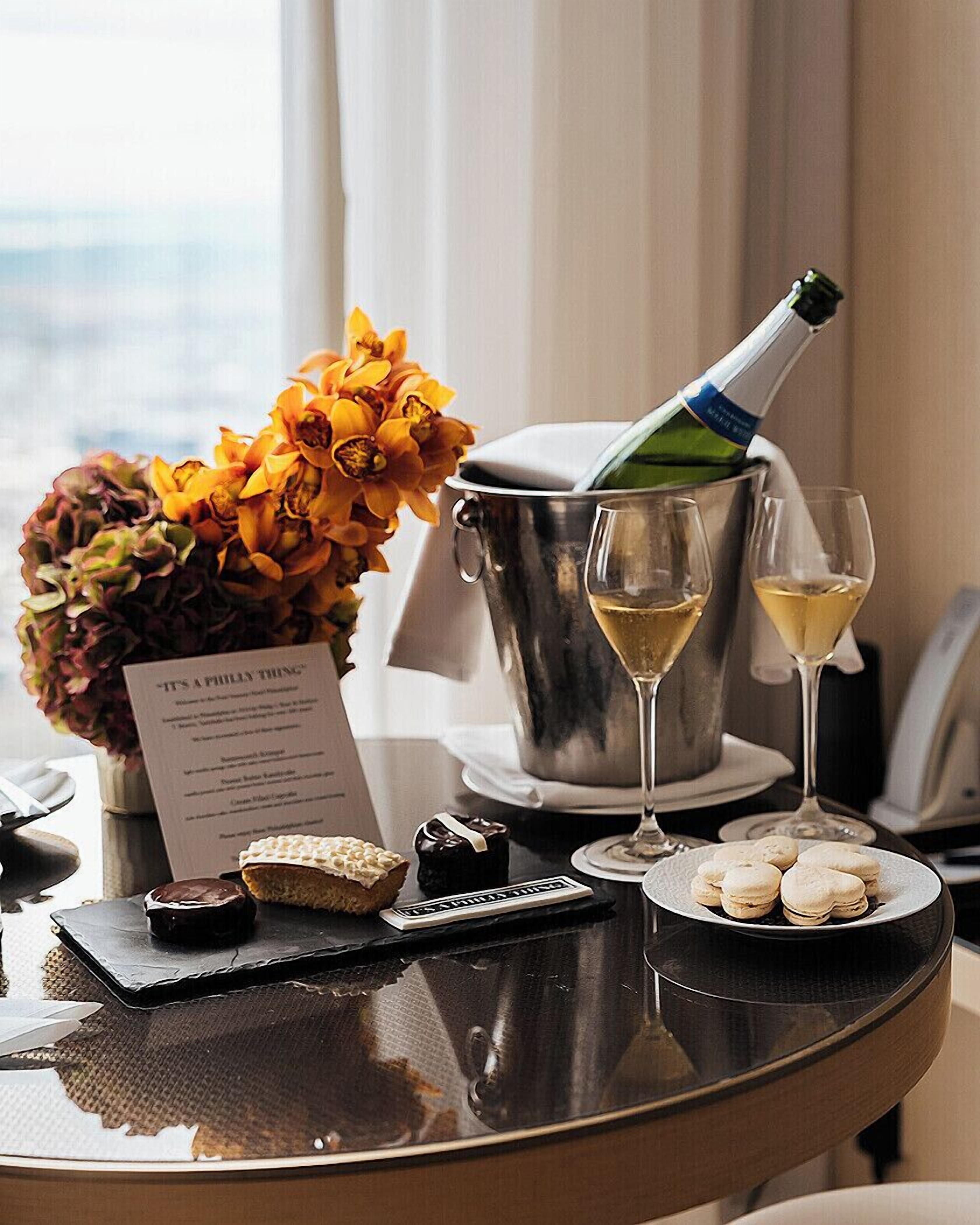 Un tavolo con una bottiglia di champagne, due calici, un bouquet di fiori, un menu e alcuni pasticcini.
