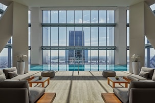 A modern lounge with a glass infinity pool, large windows, and a city view.
